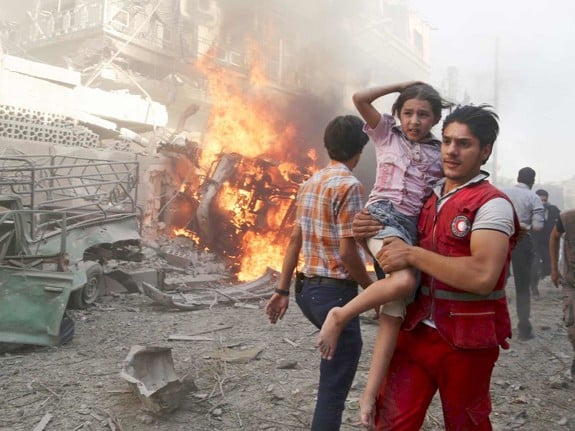 En syrisk röda korset-frivillig som springer genom rasmassor med en flicka i famnen. Det brinner i bakgrunden.