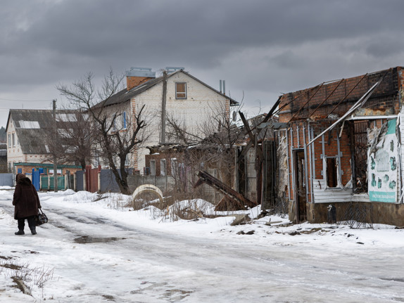 En gata i ett bostadsområde i Sumy i nordöstra Ukraina. Det är snö på marken och vädret är mulet. På gatan promenerar människor, ett av husen längs gatan är förstört efter en attack mot staden.
