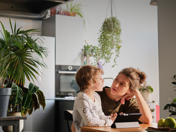 En lerfigur av ett barn med grön regnjacka i ett fönster.