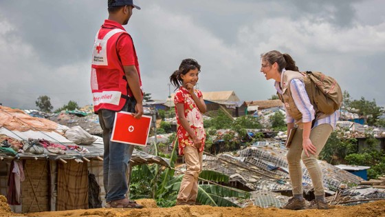 Flicka ler stort intill två vuxna volontärer i Bangladesh.