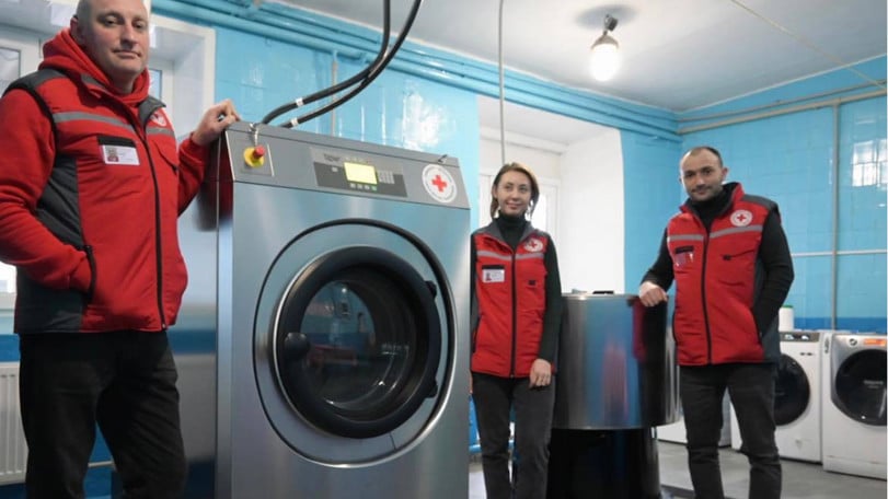Tre volontärer från Rödakorset står vid en av de nya tvättmaskinerna i tvättstugan.