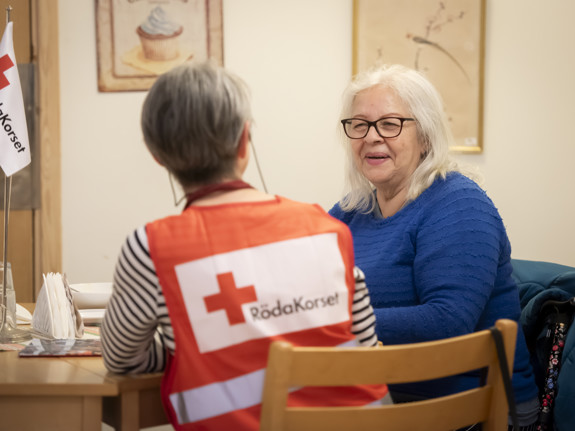En kvinnlig volontär i Röda Kors-väst samtalar med en kvinnlig stödsökande i blå kofta.