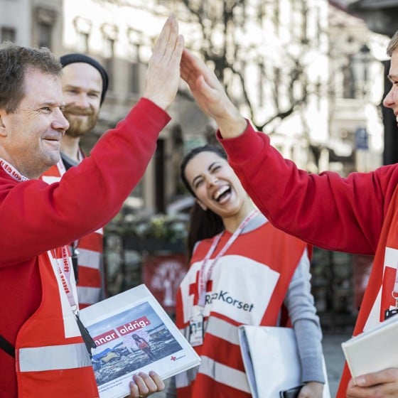 Glada värvare i Svenska Röda Korset-kläder gör en high five.