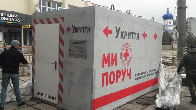 Två personer installerar ett mobilt skyddsrum gjort av betong på en gata i Cherson.