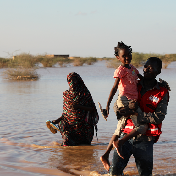Röda kors-frivillig bär barn genom vatten.