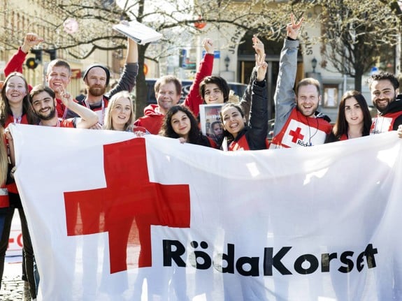 Glada värvare står bakom en Svenska Röda Korset-flagga och jublar in i kameran.