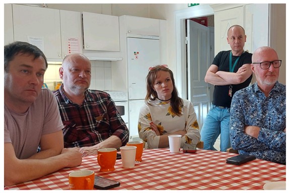 Personer som sitter och lyssnar vid bordet.