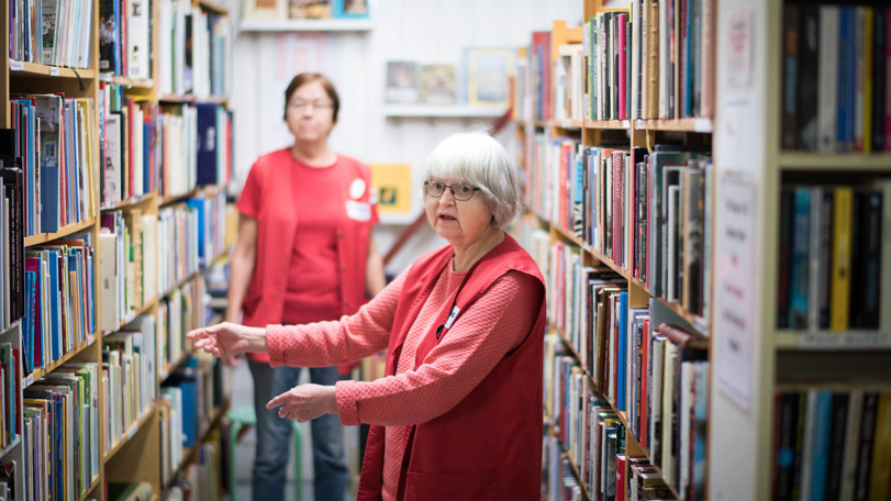 två-volontärer-står-vid-bokhyllor-fyllda-med-böcker-i-butiken