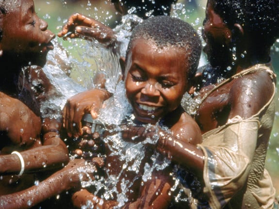 Tre barn leker med vatten. Det stänker vatten överallt.