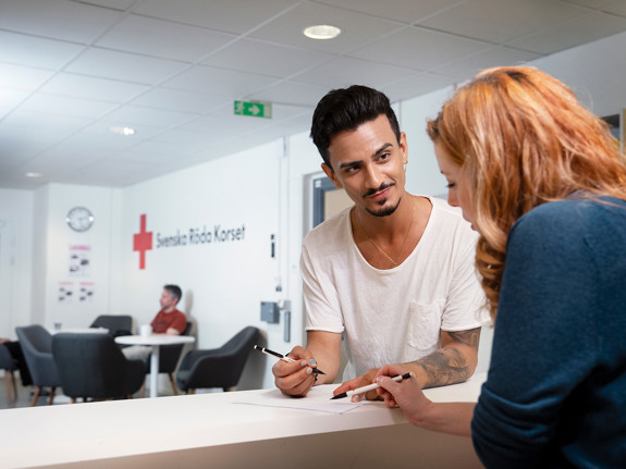 Två personer som har en dialog i receptionen på RKC i Malmö. Mannen står vänd mot fotografen och kvinnan står med ryggen mot fotografen.