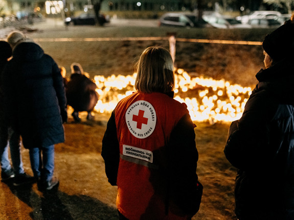 Krisstödjare från Röda Korset står framför informationsskylt med budskapet