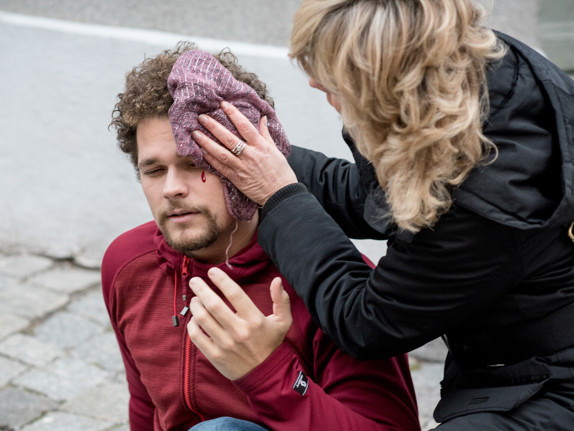 Man med skallskada får hjälp på trottoar