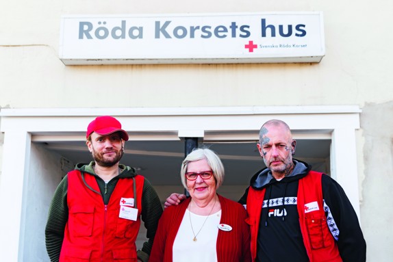 Tre rödakorsare står tillsammans framför Röda Korsets hus och tittar in i kameran.
