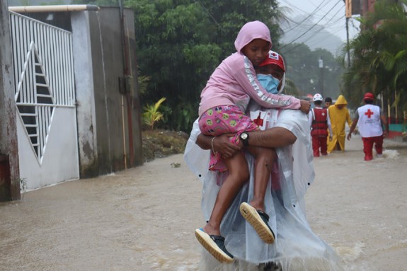 Röda Korset-volontär bär barn genom översvämning