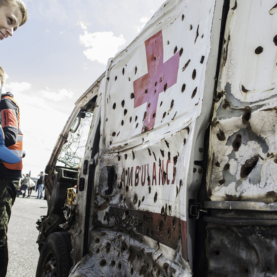 Mamma med barn tittar på skottskadad ambulans.