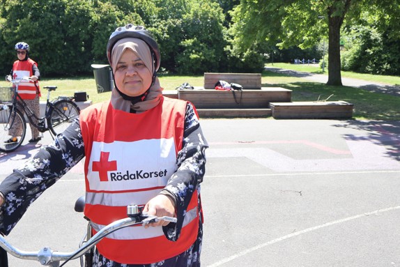 Volontär i Röda Korsets cykelskola står med cykel utomhus en solig dag