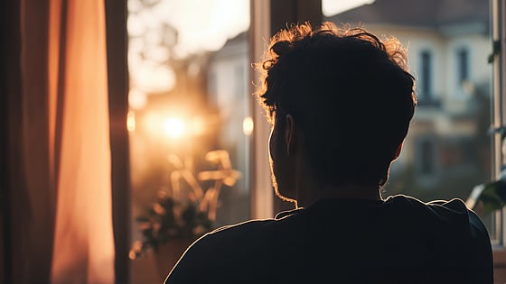Man i sorg sitter och kollar ut genom fönstret mot solen