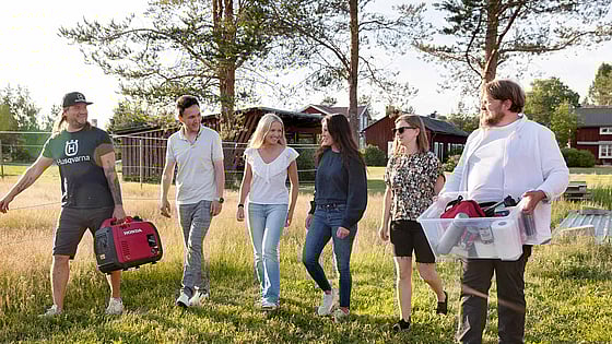 Personer bär på krislåda på en solig gräsmatta.