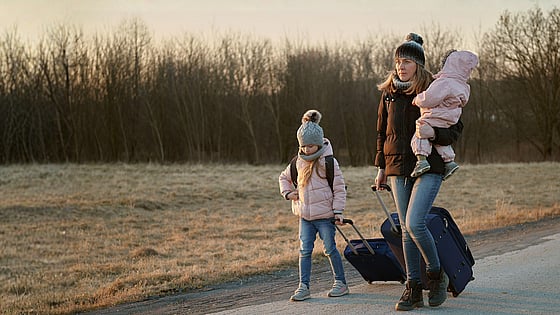 Mamma och barn går med resväskor på en väg