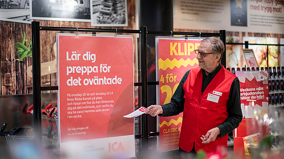 En volontär från Röda Korset i röd väst delar ut flyers med information.