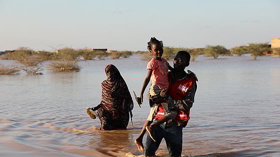 Röda kors-frivillig bär barn genom vatten.