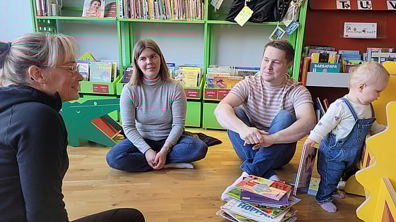 Två föräldrar sitter på golvet tillsammans med en utbildare i första hjälpen och deras barn, som leker intill.