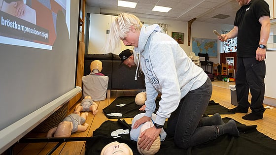 En person övar på hjärt-lungräddning på en docka. Instruktioner ges från en film som visas på väggen och stöd ges av en övningsledare som är med.