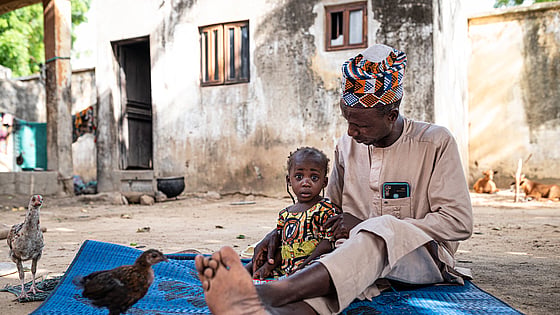 Pappa Nasiru sitter med sin dotter på en filt i Nigeria.