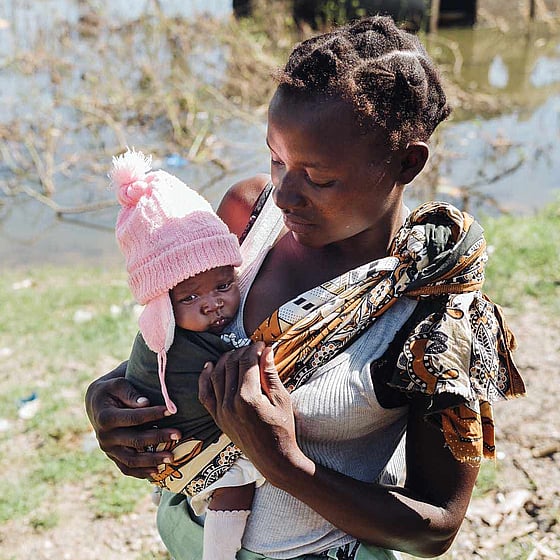 Mor bär på spädbarn i rosa mössa