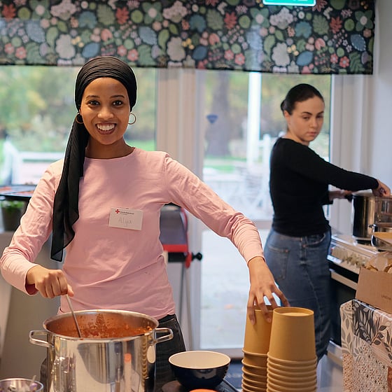 Ung kvinna serverar soppa ur stor kastrull.