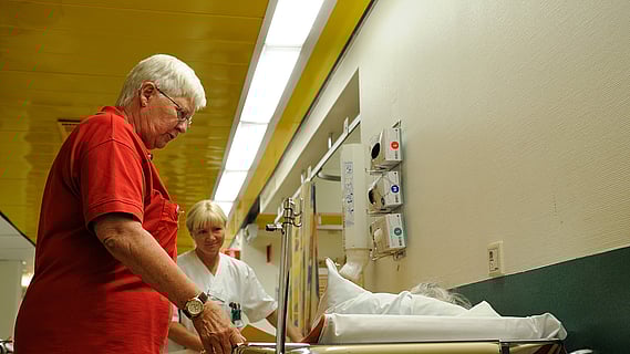 Rödakorsvärd stöttar en senior på sjukhus.