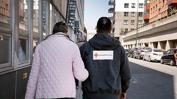 En senior går armkrok med en av Röda Korsets volontärer.