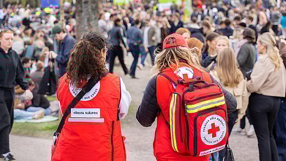 Två personer med rödakorsvästar står intill en folksamling under valborgsfirande