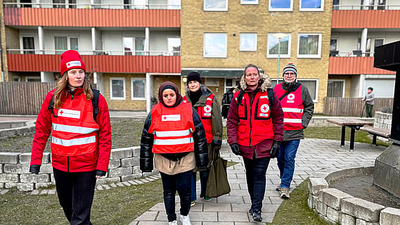 fem volontärer från Malmökretsens beredskapsgrupp är iklädda västar och går tillsammans över en gård utanför ett lägenhetshus. 
