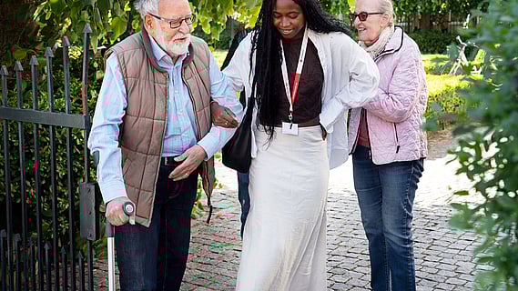 Ung kvinna som föreställer volontär är ute och går med äldre man med krycka, som föreställer deltagare. 