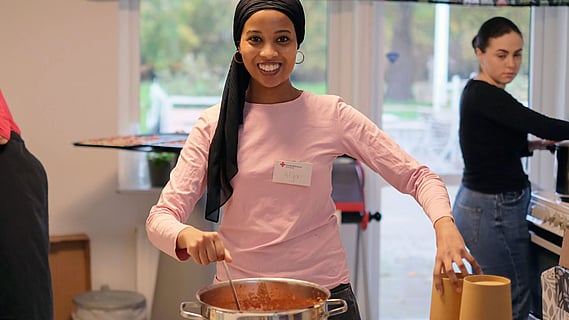 bild på kvinna som står vid kastrull redo att servera mat. 