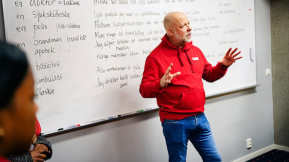 En lärare framför tavlan med svenska ord från dagens lära-svenska-grupp. 