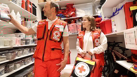 Bild av en man och kvinna iklädda första hjälpen kläder ståendes i första hjälpen gruppens förråd. 