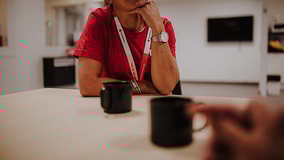 bord med kaffekoppar, kvinna med rödakors-nyckelband synd i bakgrunden. 