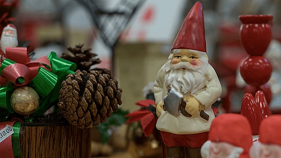 Juldekorationer på ett bord med en tomtefigur, kottar och röda prydnader.