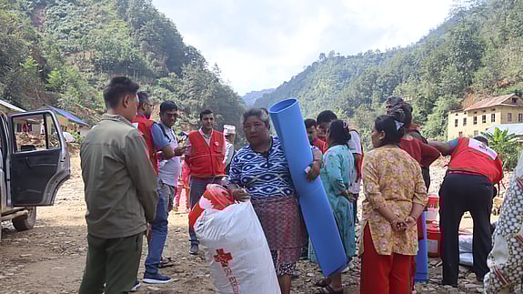 Kvinna håller i förnödenheter som hon fått av Röda Korset. Människor står runtomkring henne samt några volontärer från Röda Korset.