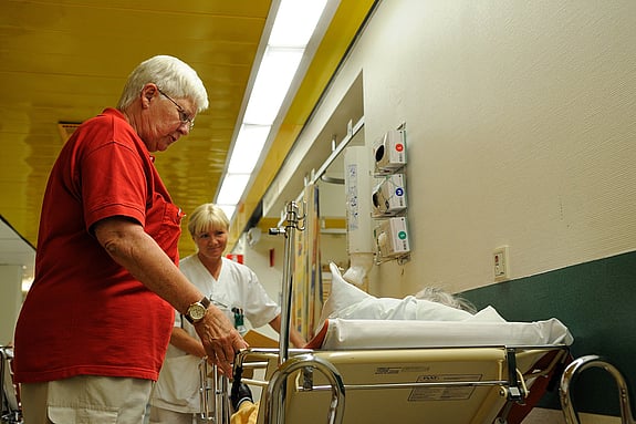 Rödakorsvärd stöttar en senior på sjukhus.