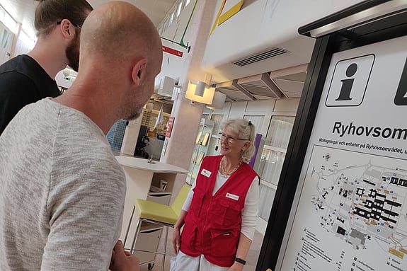 Två m'n står vid en karta och pratar med en kvinna i rödakorset-kläder.