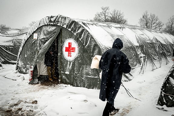 Person står framför rödakorstält. Snö ligger på marken.