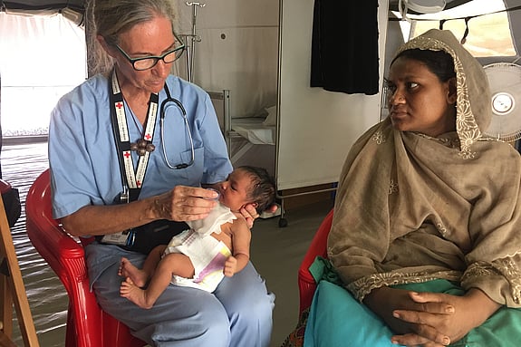 Sjukpersonal från Röda Korset håller en bebis, intill henne sitter mamman och tittar.