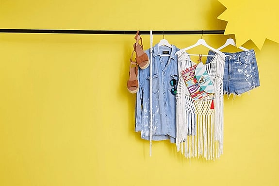 Secon hand sommarkläder är upphängda på en stång. Mot en gulbarkgrund och en sol i högra hörnet.