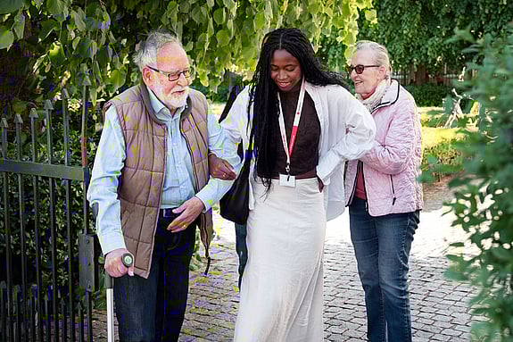 Ung kvinna som föreställer volontär är ute och går med äldre man med krycka, som föreställer deltagare. 