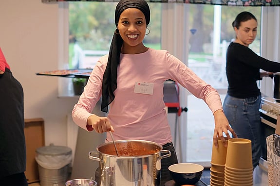 bild på kvinna som står vid kastrull redo att servera mat.