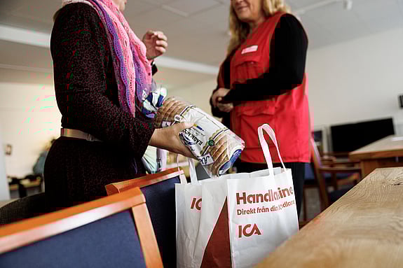 Två personer samtalar och i förgrunden syns en matkasse.