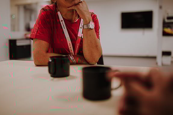 bord med kaffekoppar, kvinna med rödakors-nyckelband synd i bakgrunden.